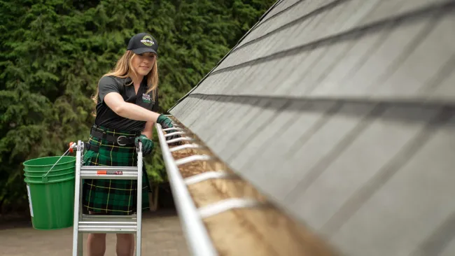 a woman on a ladder cleaning gutters