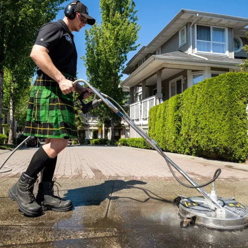 a man wearing a kilt and washing a driveway