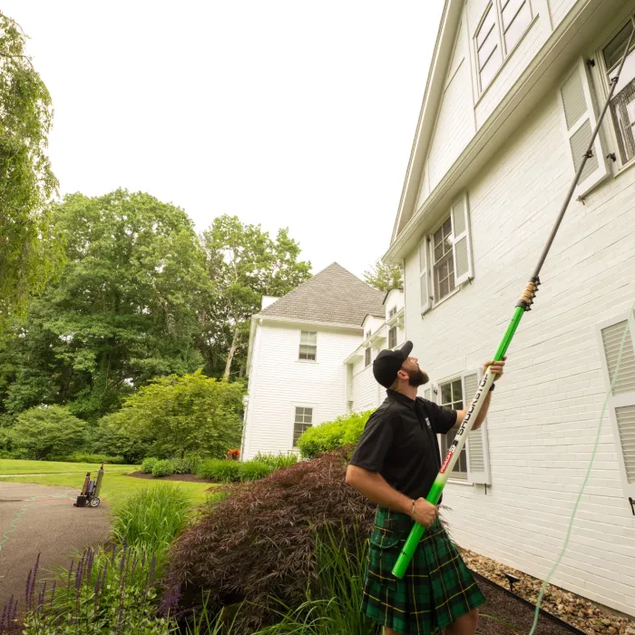 a man holding a water fed pole outside a house
