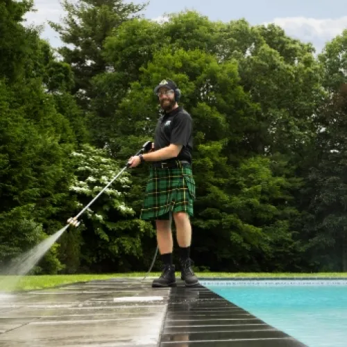 a man wearing a kilt and washing concrete by a pool