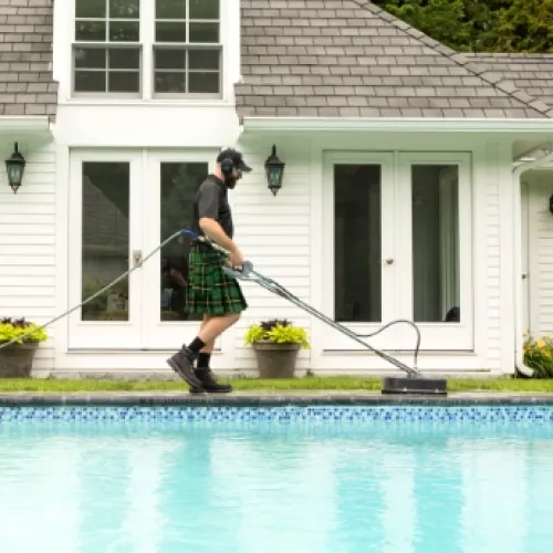 a man wearing a kilt and cleaning concrete by a pool
