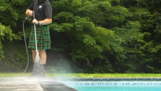 a man standing next to a pool and washing the concrete